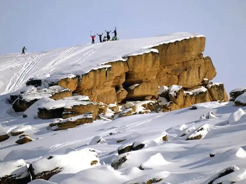 Grupo de personas en motos de nieve disfrutando la vista panorámica desde los balcones naturales durante la travesía invernal.